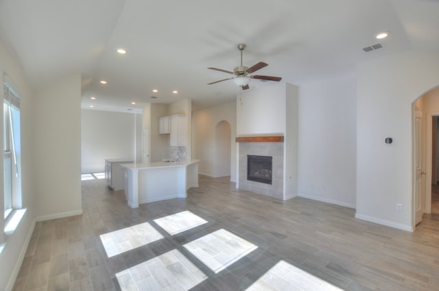 unfurnished living room with light hardwood / wood-style flooring, ceiling fan, lofted ceiling, and a tiled fireplace