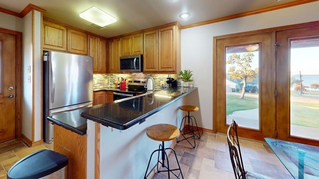 kitchen with backsplash, kitchen peninsula, a breakfast bar, appliances with stainless steel finishes, and ornamental molding