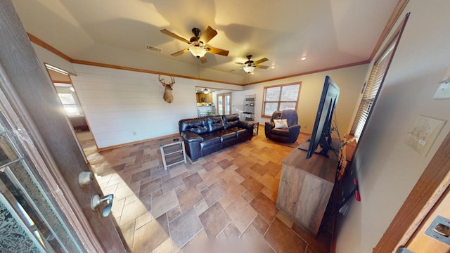 living room with ceiling fan, crown molding, and wood walls