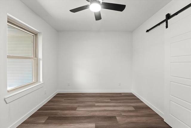 spare room with dark wood-type flooring, a barn door, and ceiling fan