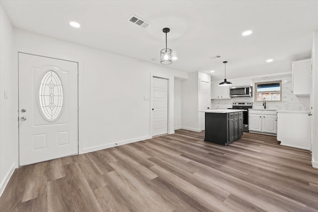 kitchen with appliances with stainless steel finishes, decorative light fixtures, white cabinets, hardwood / wood-style flooring, and a center island