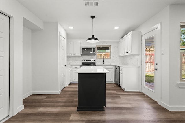 kitchen with appliances with stainless steel finishes, pendant lighting, white cabinetry, backsplash, and a center island