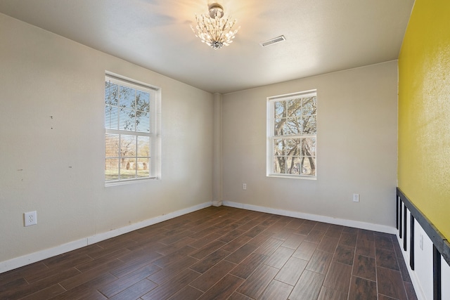 spare room with dark hardwood / wood-style floors and a notable chandelier