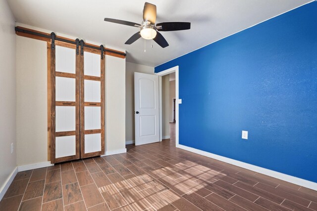 spare room with a barn door, ceiling fan, and dark hardwood / wood-style flooring