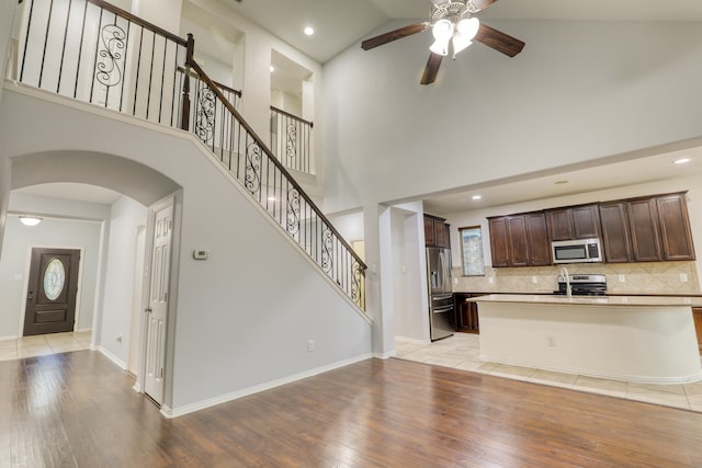 kitchen featuring high vaulted ceiling, ceiling fan, dark brown cabinets, light hardwood / wood-style floors, and stainless steel appliances