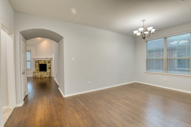 spare room with a notable chandelier, a stone fireplace, and dark wood-type flooring