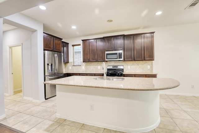 kitchen with sink, stainless steel appliances, light stone counters, a kitchen island with sink, and dark brown cabinets