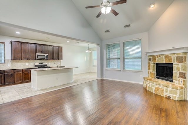 kitchen featuring sink, stainless steel appliances, a stone fireplace, backsplash, and light hardwood / wood-style floors