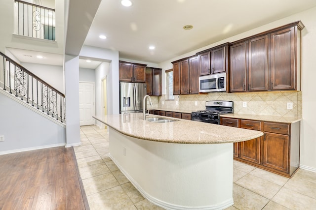 kitchen with light stone countertops, appliances with stainless steel finishes, light wood-type flooring, sink, and a center island with sink