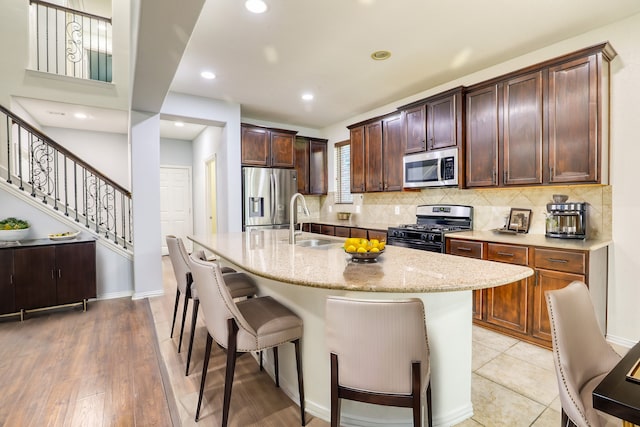 kitchen with sink, a kitchen breakfast bar, an island with sink, light hardwood / wood-style floors, and appliances with stainless steel finishes