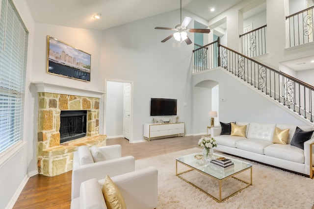 living room featuring ceiling fan, a stone fireplace, wood-type flooring, and high vaulted ceiling