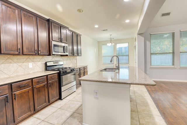 kitchen featuring appliances with stainless steel finishes, sink, a center island with sink, an inviting chandelier, and light hardwood / wood-style flooring