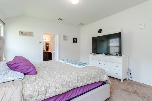 bedroom with ensuite bathroom, light carpet, and vaulted ceiling