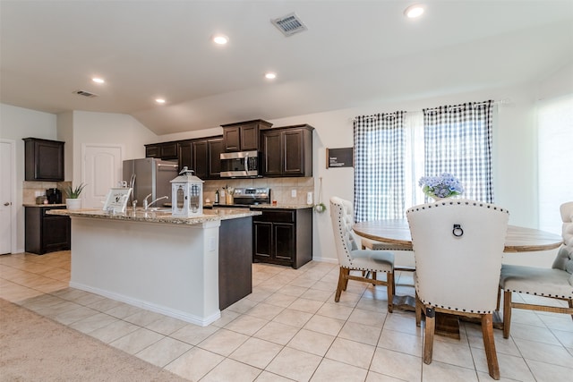 kitchen with decorative backsplash, an island with sink, light tile patterned floors, and appliances with stainless steel finishes