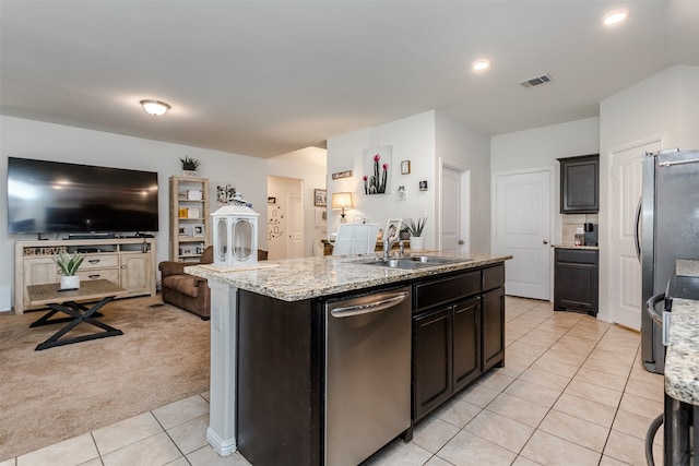 kitchen with light carpet, light stone countertops, stainless steel appliances, sink, and a center island with sink