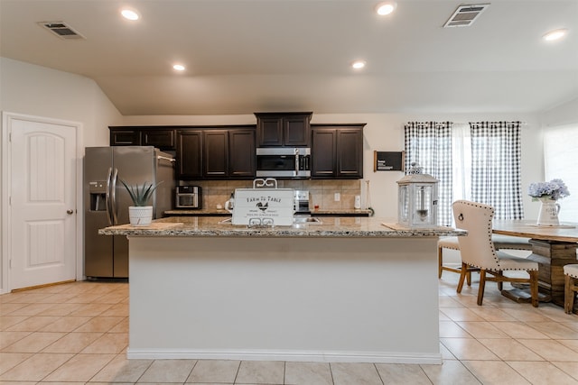 kitchen featuring a center island with sink, light tile patterned floors, stainless steel appliances, and vaulted ceiling