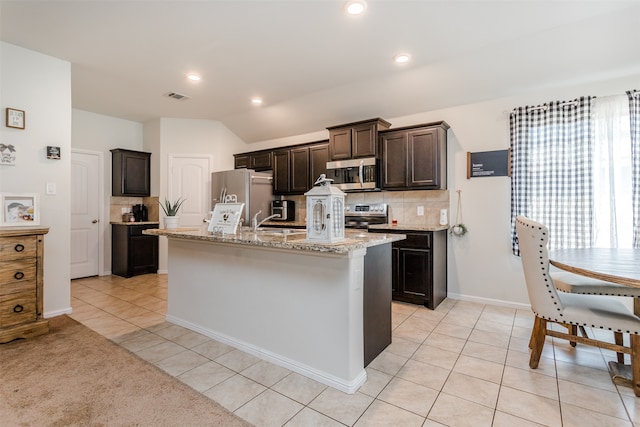 kitchen featuring appliances with stainless steel finishes, dark brown cabinetry, light tile patterned floors, and a kitchen island with sink