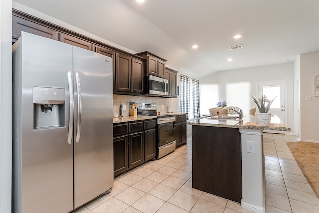 kitchen with sink, stainless steel appliances, an island with sink, vaulted ceiling, and dark brown cabinets