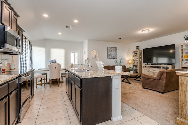 kitchen featuring light carpet, dark brown cabinets, stainless steel appliances, a kitchen island with sink, and sink