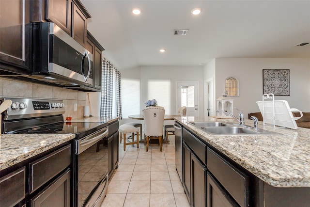 kitchen with a center island with sink, sink, decorative backsplash, light tile patterned floors, and stainless steel appliances