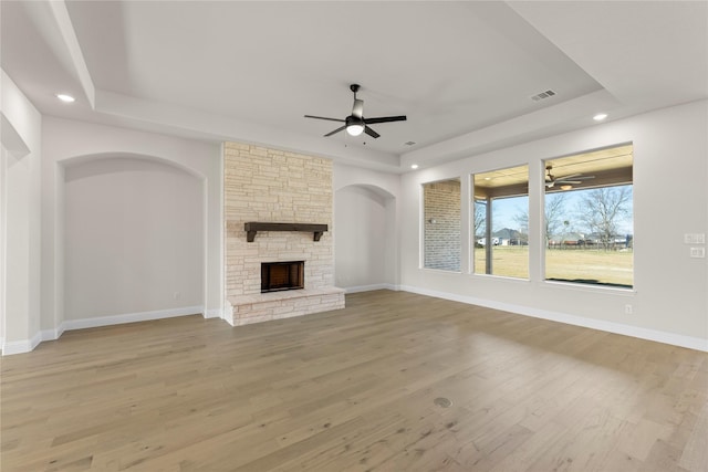 unfurnished living room with ceiling fan, a raised ceiling, a fireplace, and light hardwood / wood-style flooring