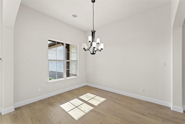 spare room with a notable chandelier and light hardwood / wood-style flooring