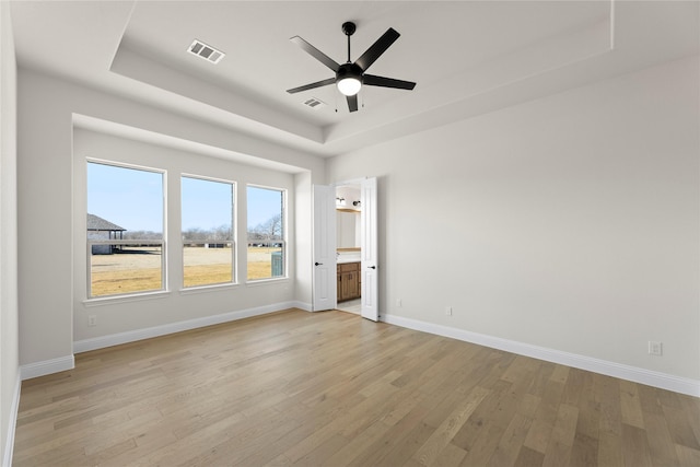 unfurnished bedroom featuring ceiling fan, ensuite bath, light hardwood / wood-style floors, and a raised ceiling