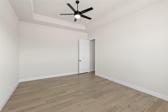 empty room featuring ceiling fan, light wood-type flooring, and a raised ceiling