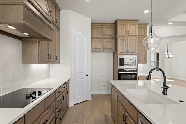 kitchen featuring sink, backsplash, custom range hood, decorative light fixtures, and black appliances