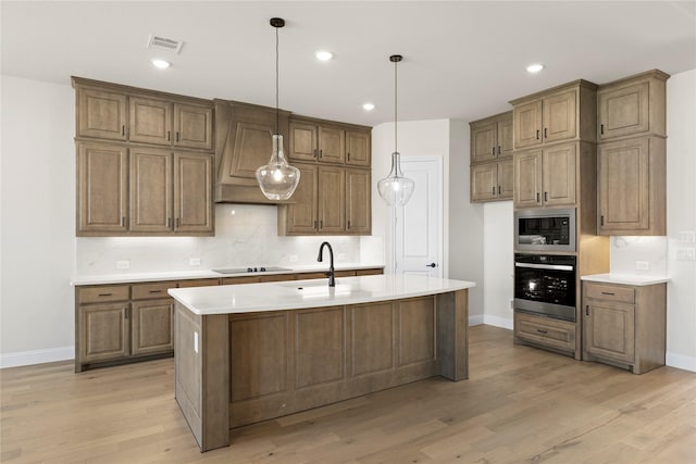 kitchen featuring oven, light hardwood / wood-style flooring, black electric cooktop, built in microwave, and an island with sink