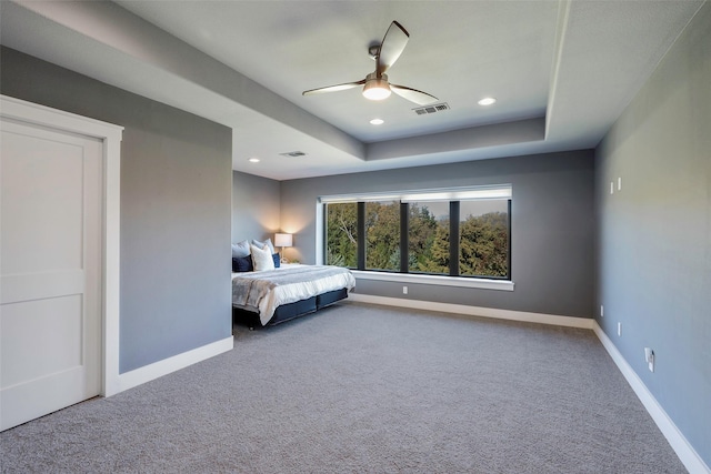 carpeted bedroom with a raised ceiling and ceiling fan