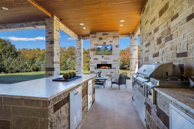 view of patio with area for grilling, a grill, and an outdoor stone fireplace