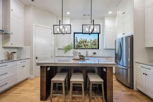 kitchen featuring white cabinetry, a kitchen breakfast bar, light stone counters, a kitchen island, and stainless steel fridge with ice dispenser