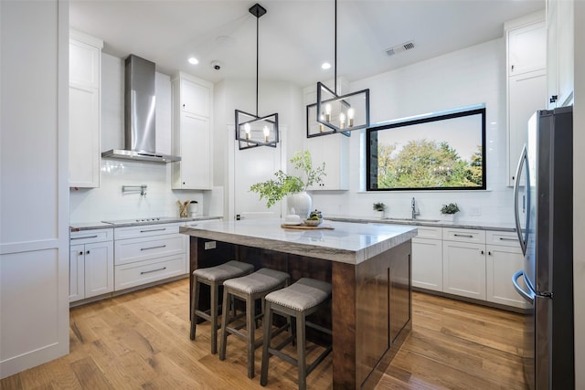 kitchen with white cabinets, stainless steel refrigerator, wall chimney exhaust hood, and a kitchen island