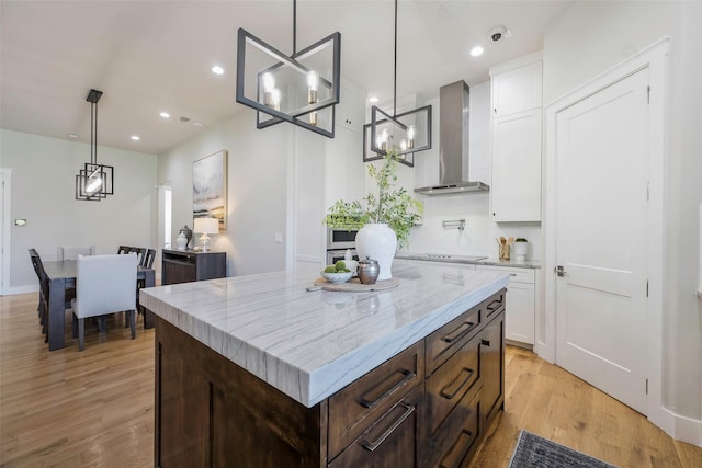 kitchen featuring white cabinetry, a center island, dark brown cabinets, hanging light fixtures, and wall chimney range hood