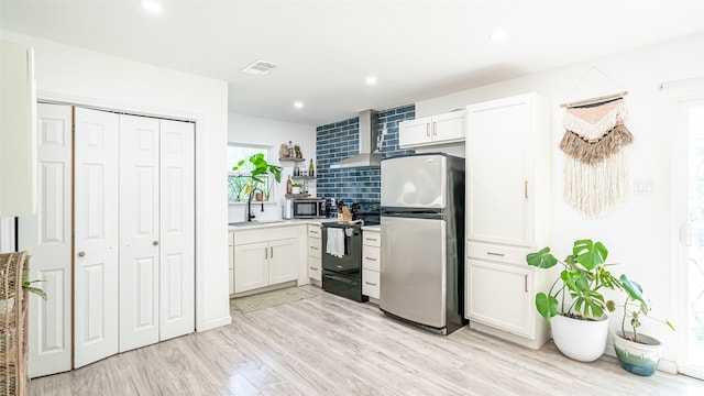 kitchen with decorative backsplash, appliances with stainless steel finishes, wall chimney exhaust hood, light hardwood / wood-style floors, and white cabinetry