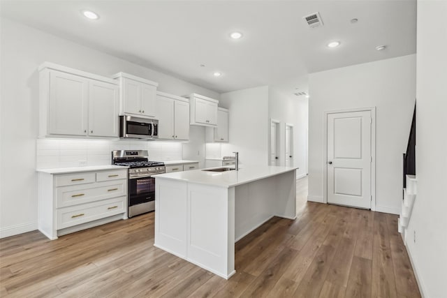 kitchen featuring appliances with stainless steel finishes, sink, decorative backsplash, light hardwood / wood-style floors, and a center island with sink