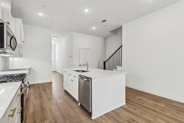 kitchen with sink, white cabinetry, light hardwood / wood-style flooring, appliances with stainless steel finishes, and a kitchen island with sink