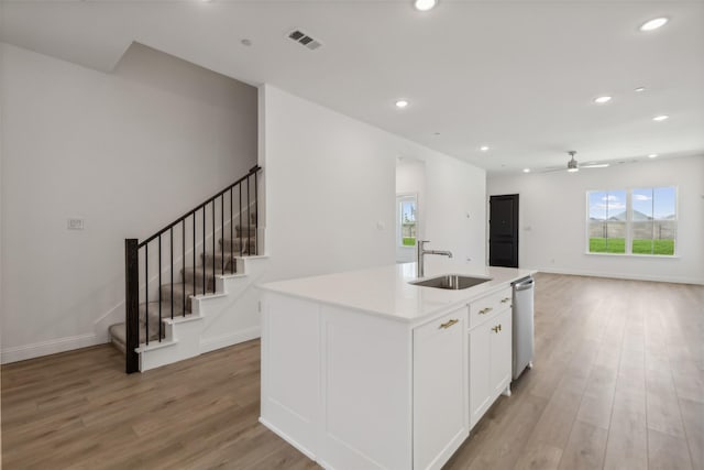 kitchen with sink, white cabinetry, light wood-type flooring, dishwasher, and an island with sink