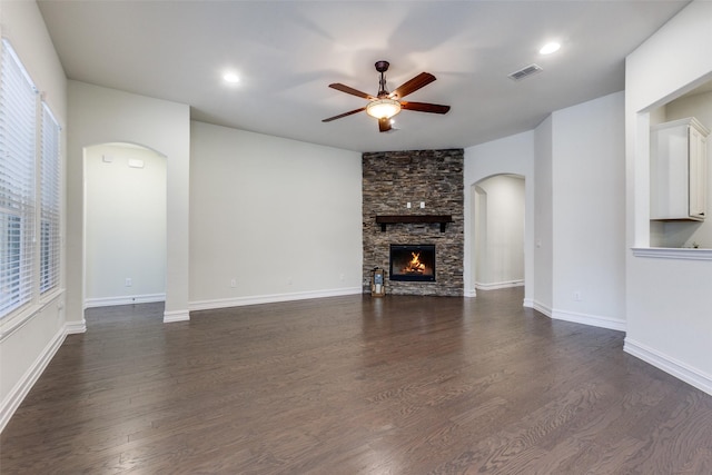 unfurnished living room with a stone fireplace, ceiling fan, and dark wood-type flooring