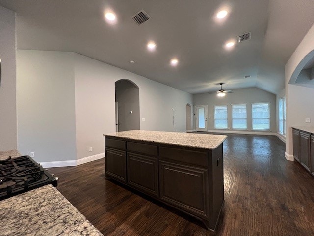 kitchen featuring dark wood-type flooring, dark brown cabinets, a center island, light stone countertops, and vaulted ceiling