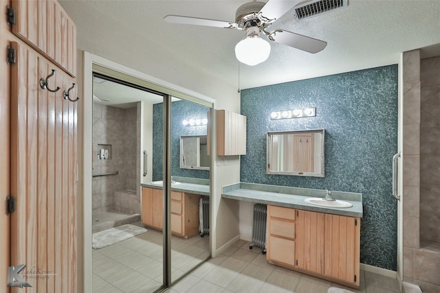 bathroom with tiled shower, radiator, vanity, and ceiling fan