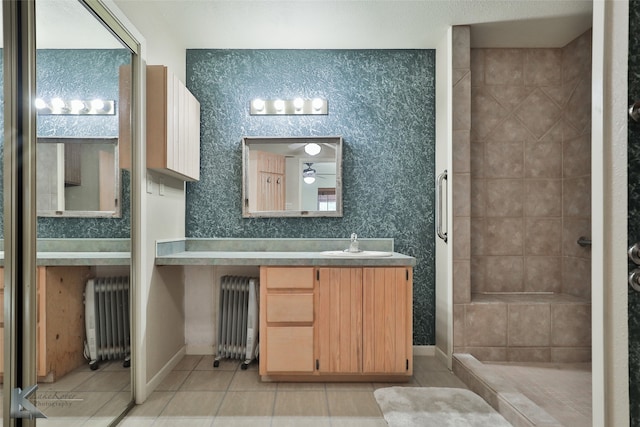 bathroom featuring tile patterned flooring, vanity, a tile shower, and radiator