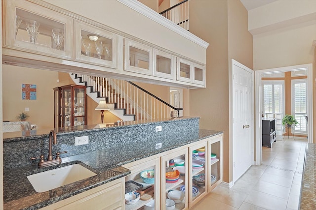 interior space with light tile patterned flooring, a towering ceiling, dark stone countertops, and sink