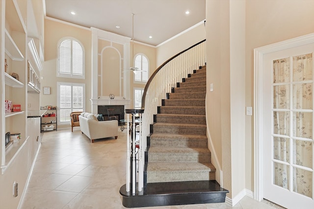 staircase featuring tile patterned flooring, a towering ceiling, a healthy amount of sunlight, and ornamental molding