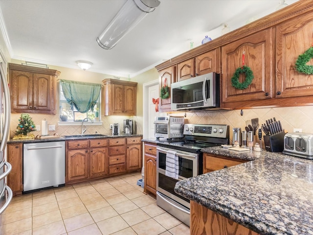 kitchen featuring sink, stainless steel appliances, dark stone countertops, light tile patterned flooring, and ornamental molding