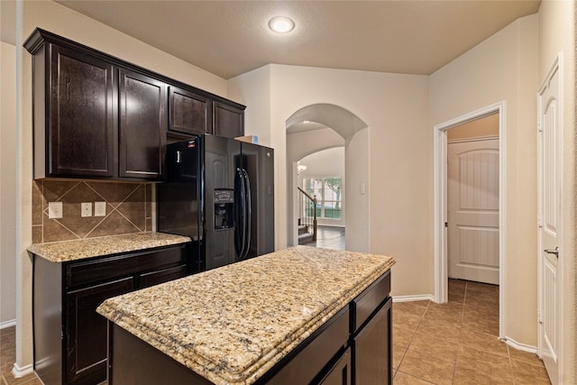 kitchen featuring black fridge, light stone counters, backsplash, dark brown cabinets, and a kitchen island