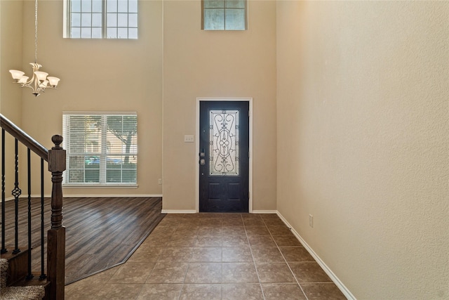 foyer with a wealth of natural light, tile patterned flooring, a towering ceiling, and an inviting chandelier