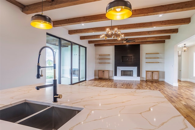 kitchen with a large fireplace, sink, beam ceiling, light hardwood / wood-style floors, and hanging light fixtures