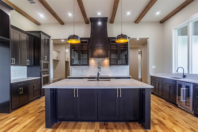 kitchen with tasteful backsplash, light stone counters, light hardwood / wood-style flooring, decorative light fixtures, and custom range hood